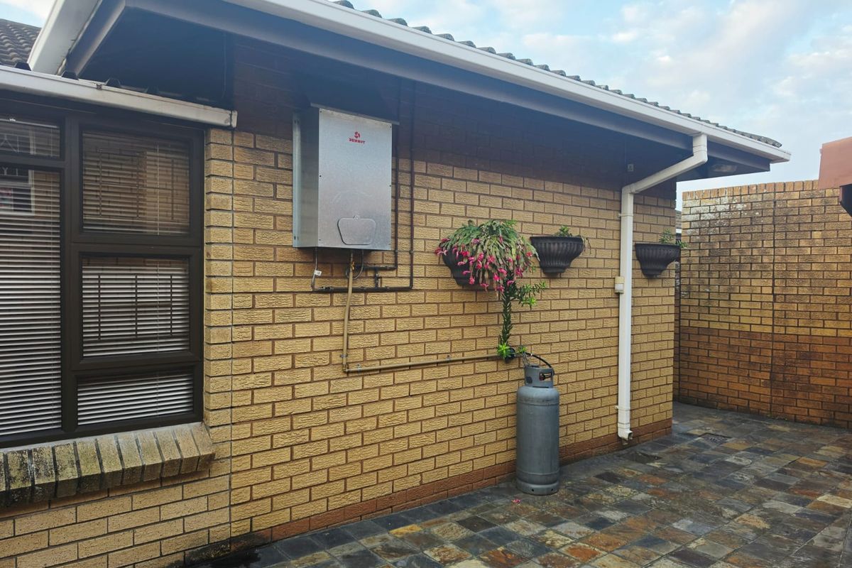 Rear exterior view of the townhouse featuring a brick facade, gas geyser installation, and paved patio area.