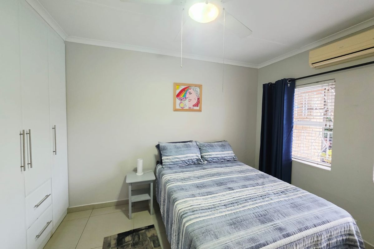 A well-maintained bedroom featuring built-in cupboards, tiled flooring, a ceiling fan, and a wall-mounted air conditioning unit.