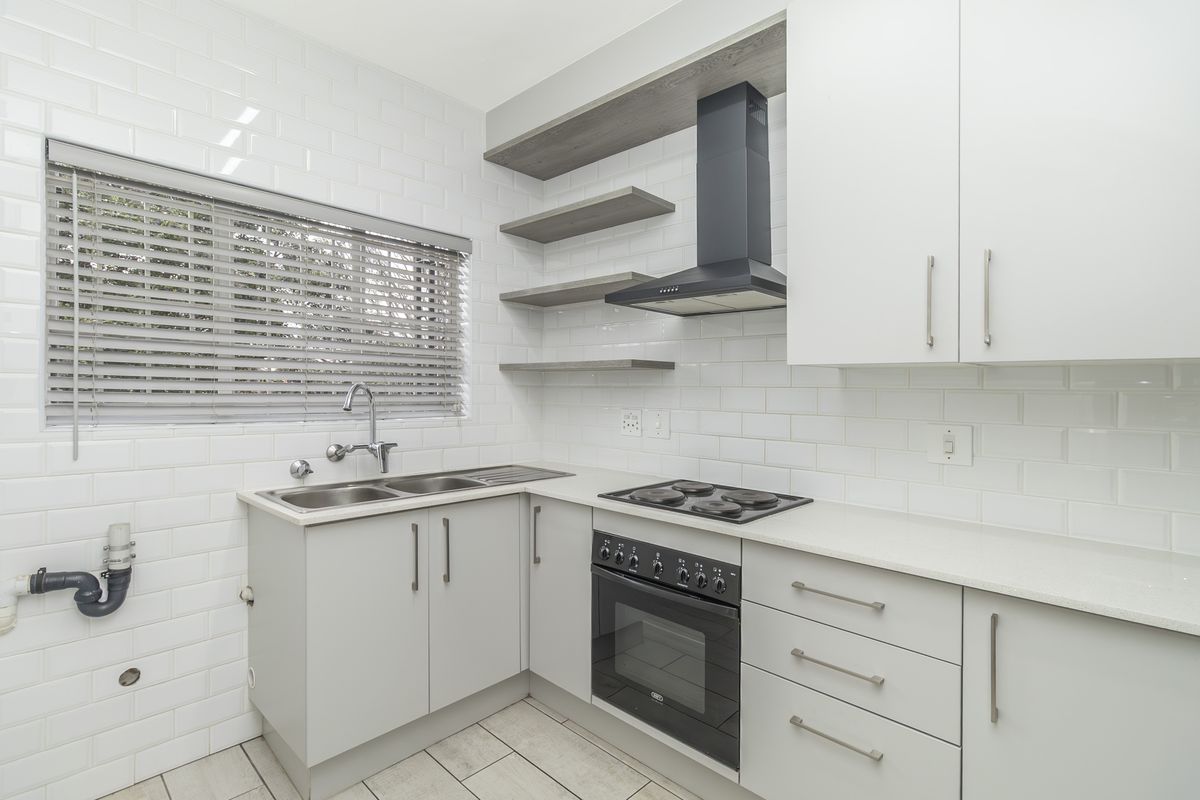 Modern kitchen featuring white subway tile backsplash, light grey cabinetry, stone countertops, built-in oven, electric hob, and a stainless steel double sink.