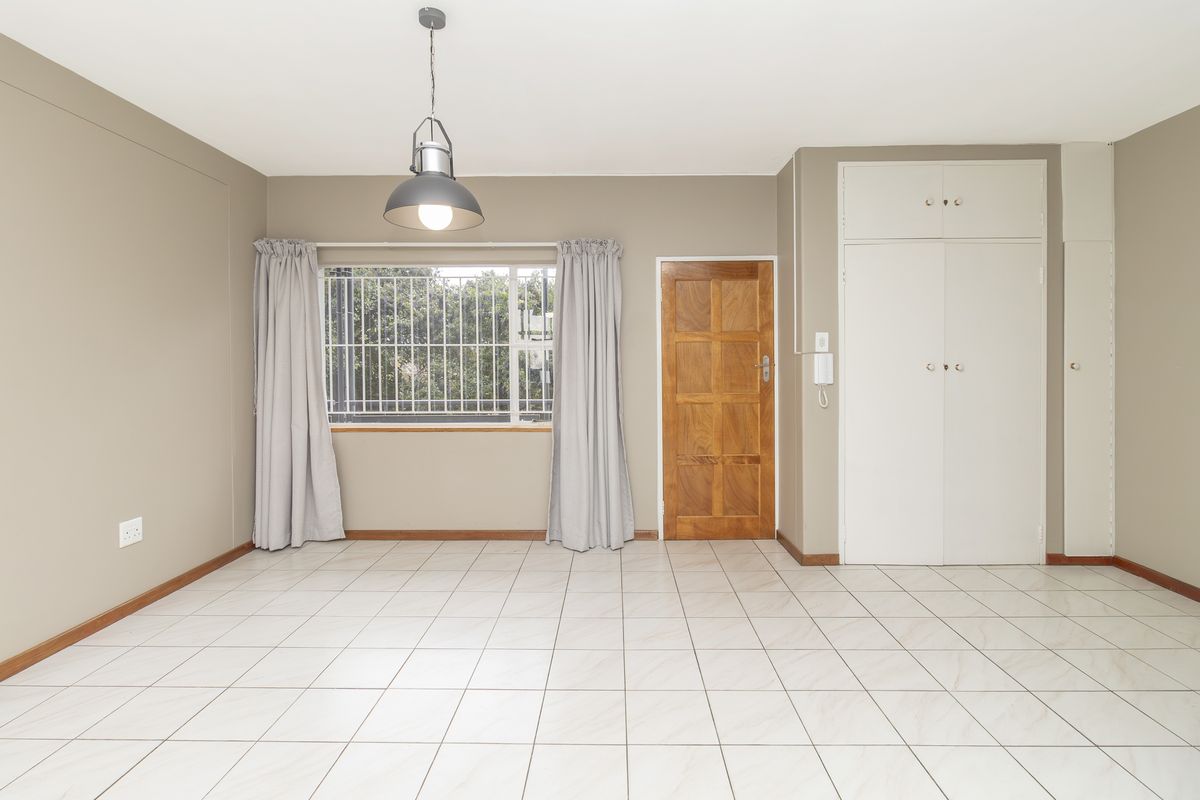 A spacious, empty bedroom featuring neutral wall tones, tiled flooring, built-in storage cupboards, and a wooden entrance door.