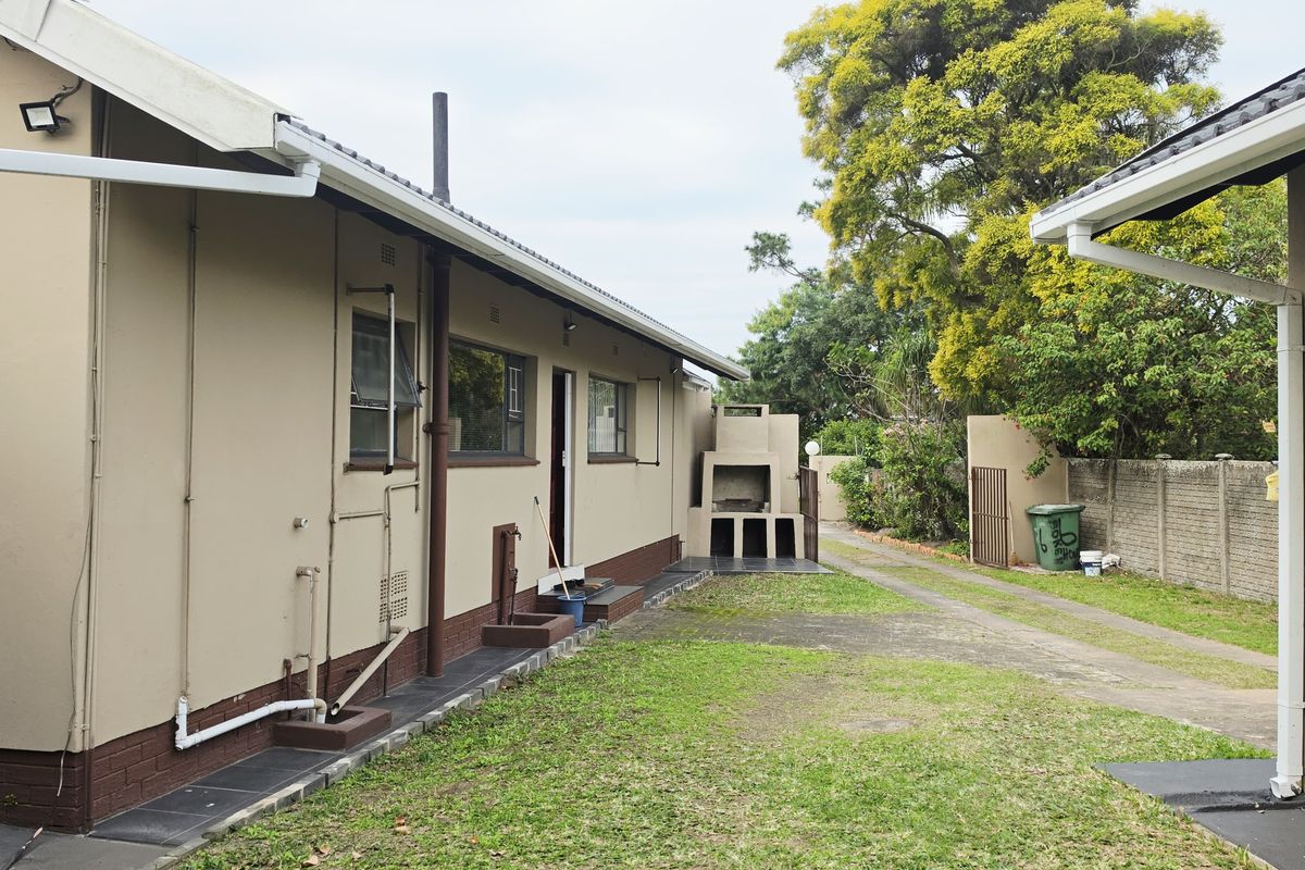 Rear exterior view of the property featuring a paved driveway, lawn area, and a built-in outdoor braai facility.