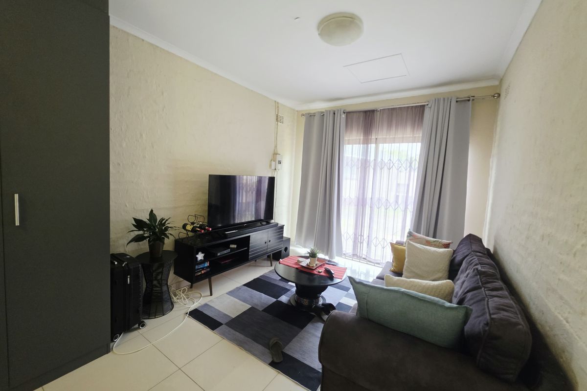 A living room featuring tiled flooring, a built-in cupboard, and a sliding glass door with a security gate leading to the exterior.