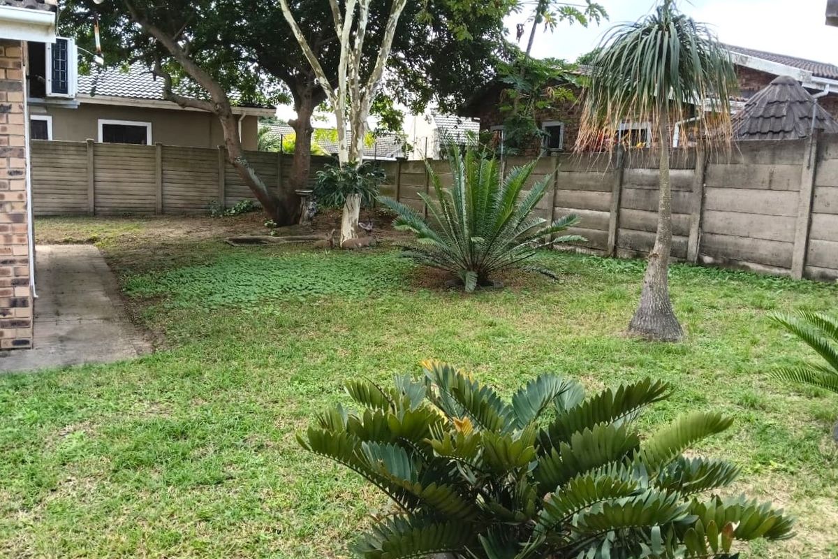 A private rear garden featuring a lawn, established trees, cycad plants, and a precast concrete boundary wall.