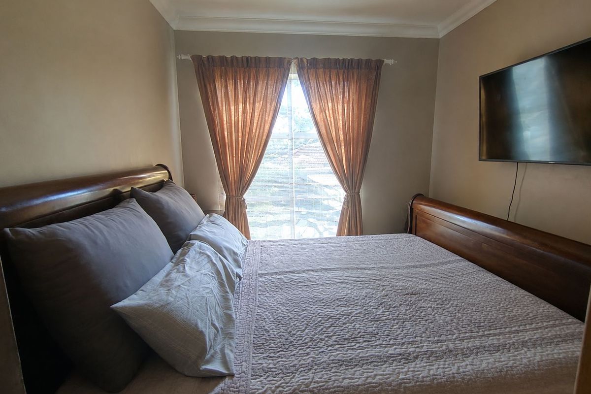A cozy bedroom featuring neutral wall tones, coving, and a window with curtains, providing a comfortable and functional sleeping space.