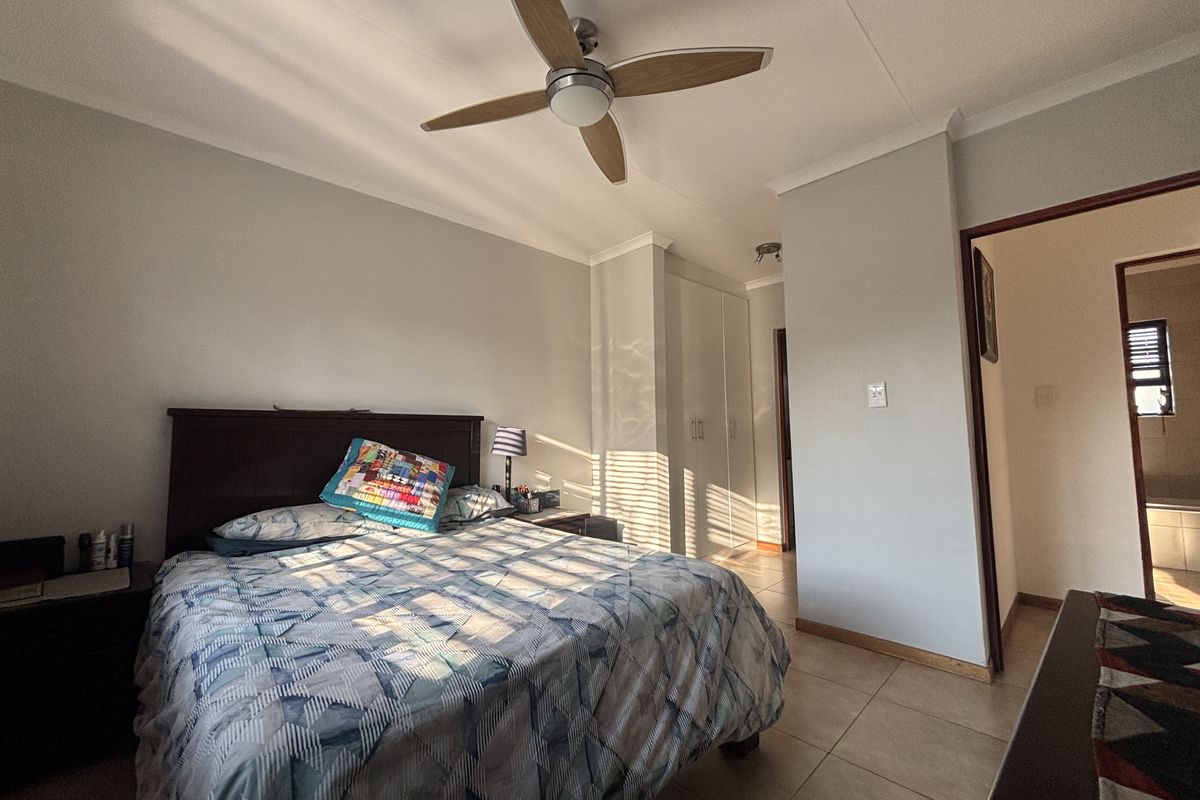 A well-maintained bedroom featuring tiled flooring, built-in cupboards, and a modern ceiling fan, with natural light filtering through the window.