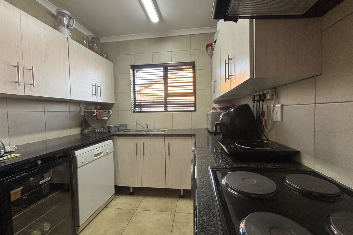Functional kitchen featuring light wood cabinetry, granite countertops, tiled backsplash, and integrated electric hob with extractor fan.