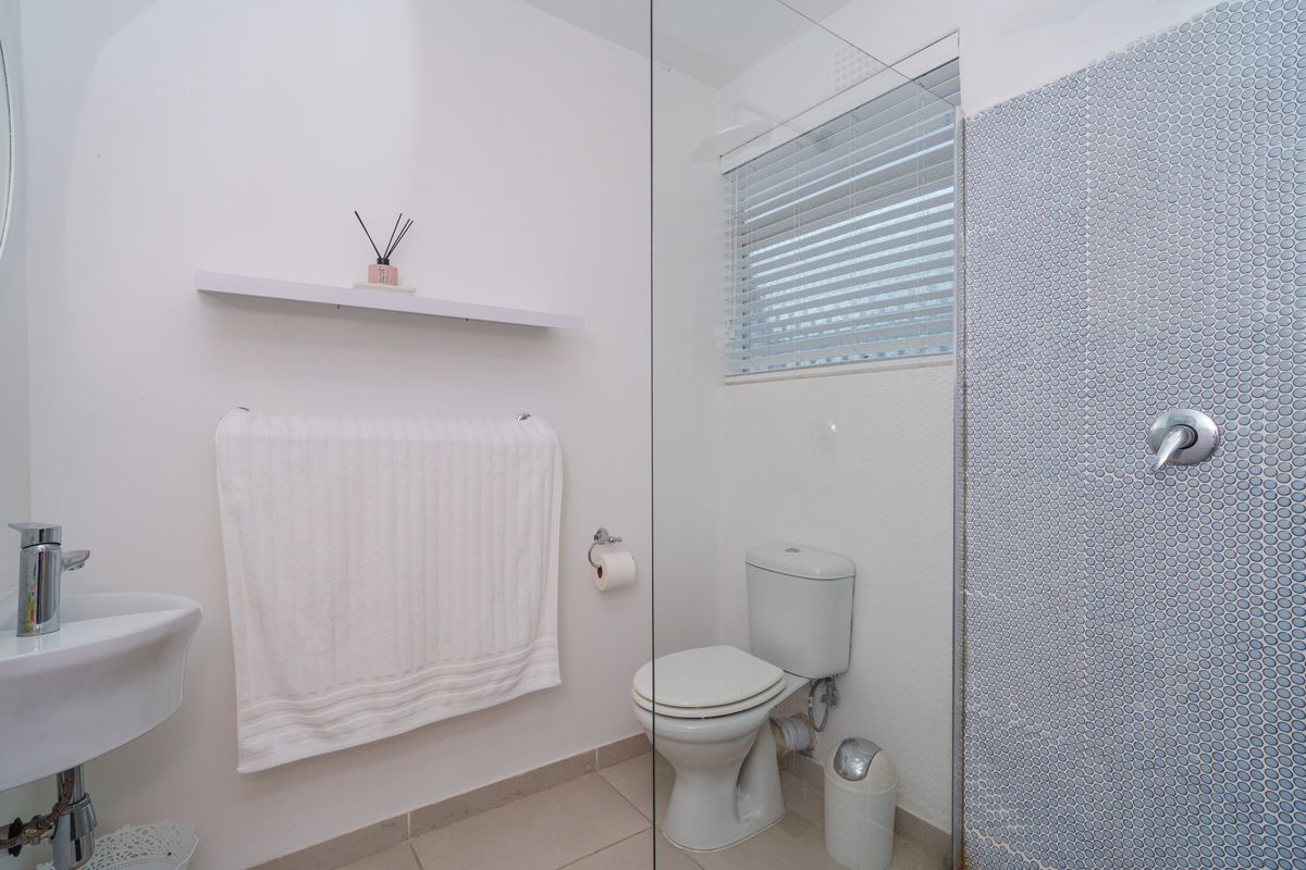 A clean and functional bathroom featuring a wall-mounted basin, a toilet, and a glass-enclosed shower area with a decorative mosaic tile accent wall.