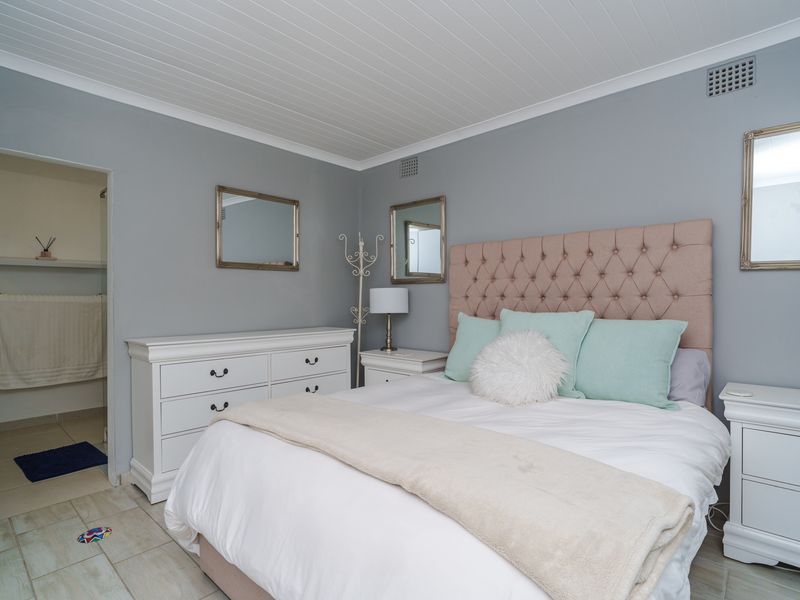 A well-maintained bedroom featuring light grey walls, a tongue and groove ceiling, and tiled flooring, with an adjoining en-suite bathroom.