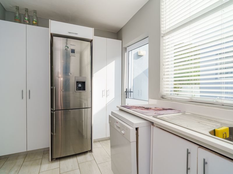 A functional scullery featuring white built-in cabinetry, a stainless steel sink, tiled flooring, and direct access to the exterior.