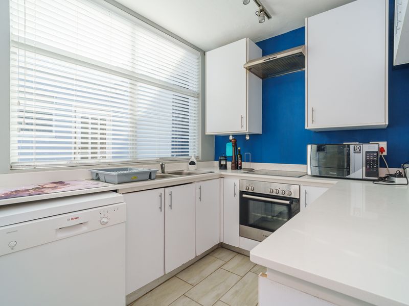 A functional kitchen featuring white cabinetry, stone countertops, stainless steel appliances, and tiled flooring, illuminated by a large window with venetian blinds.