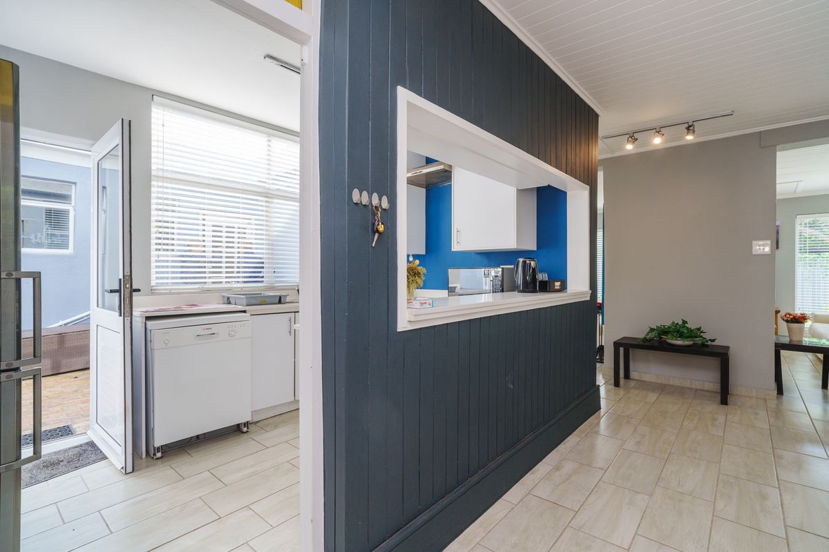 A functional kitchen featuring a pass-through window, dark panelled feature wall, tiled flooring, and built-in cabinetry with integrated appliances.