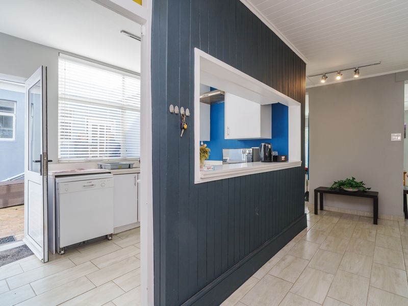 A functional kitchen featuring a pass-through window, dark panelled feature wall, tiled flooring, and built-in cabinetry with integrated appliances.