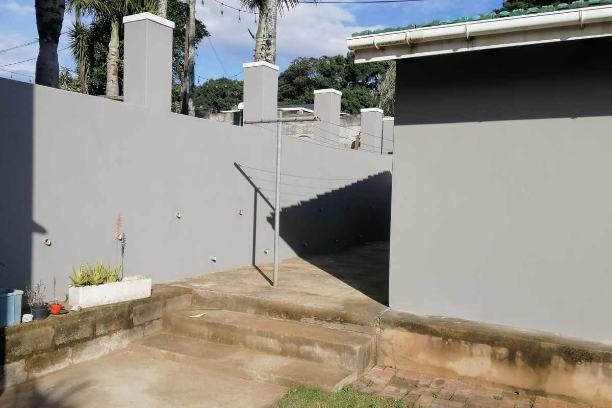A rear exterior view showing a concrete pathway, steps, and a perimeter wall with integrated pillars and a fixed washing line.