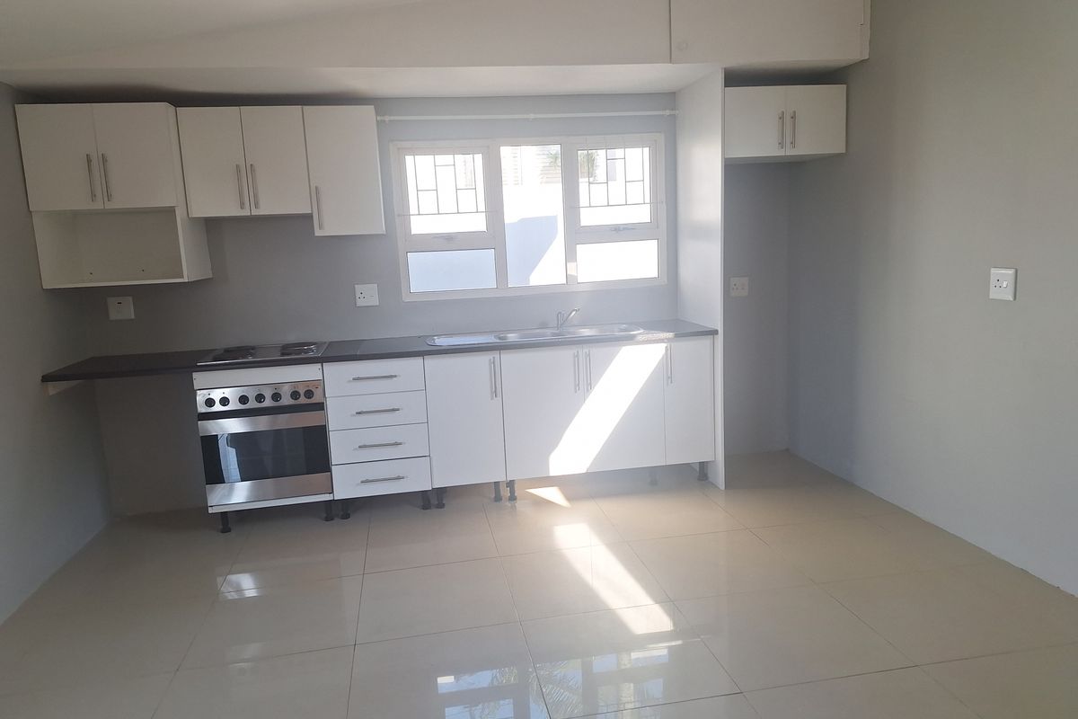 A clean, modern kitchen featuring white cabinetry, a built-in oven and hob, stainless steel sink, and polished floor tiles.