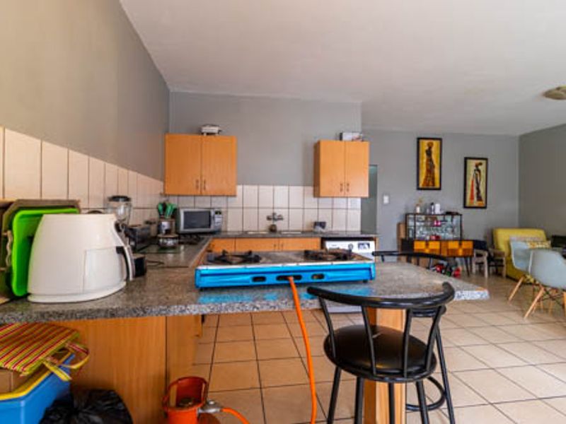 Open-plan kitchen and living area featuring laminate cabinetry, granite countertops, tiled backsplash, and ceramic floor tiles throughout.