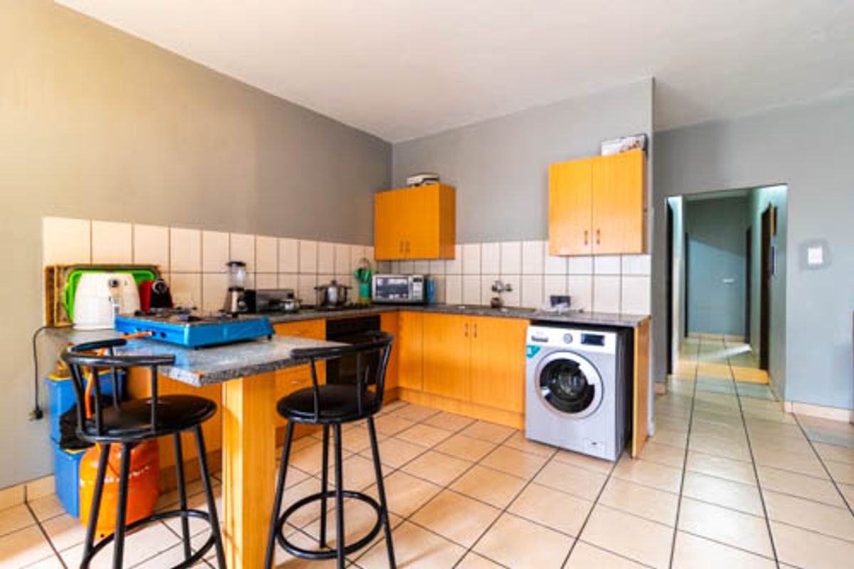 Functional kitchen featuring laminate cabinetry, tiled backsplash, stone countertops, and an integrated washing machine, with direct access to the hallway.