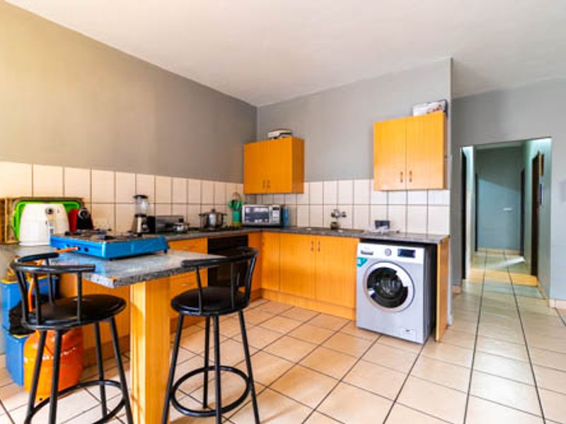 Functional kitchen featuring laminate cabinetry, tiled backsplash, stone countertops, and an integrated washing machine, with direct access to the hallway.