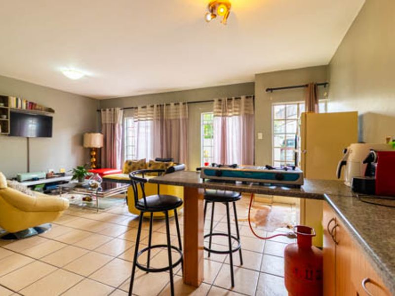 An open-plan living and kitchen area featuring tiled flooring, a breakfast bar, and functional cabinetry, offering a versatile space for daily living.