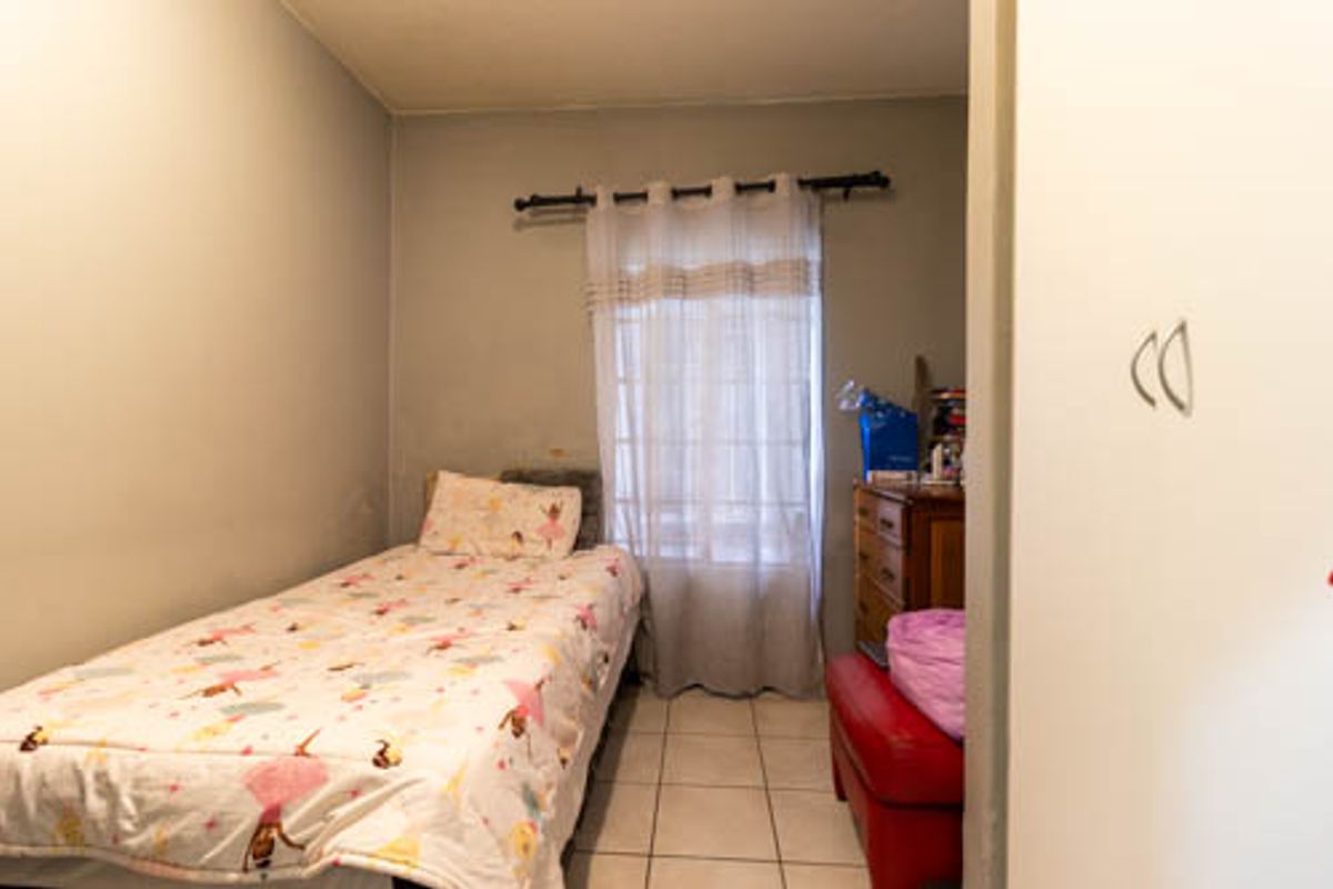 A compact bedroom featuring tiled flooring and a window with a curtain rod, offering a functional space for a single bed.