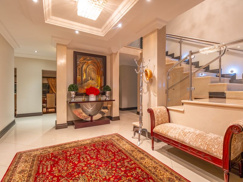 Elegant entrance hall featuring polished porcelain flooring, a grand stone staircase with glass balustrades, and sophisticated recessed ceiling lighting.