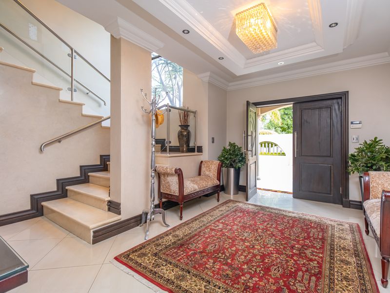 Elegant entrance foyer featuring a grand staircase with glass balustrades, high-quality tiled flooring, and a sophisticated recessed ceiling design.