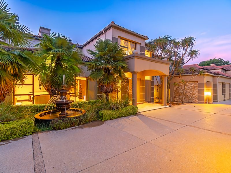 A well-maintained cluster home exterior featuring a paved driveway, covered entrance porch, stone feature wall, and a decorative water fountain in the front garden.