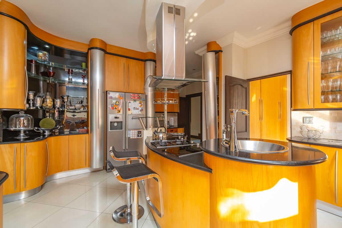 A spacious kitchen featuring warm wood-toned cabinetry, granite countertops, a central island with a built-in hob, and modern stainless steel appliances.