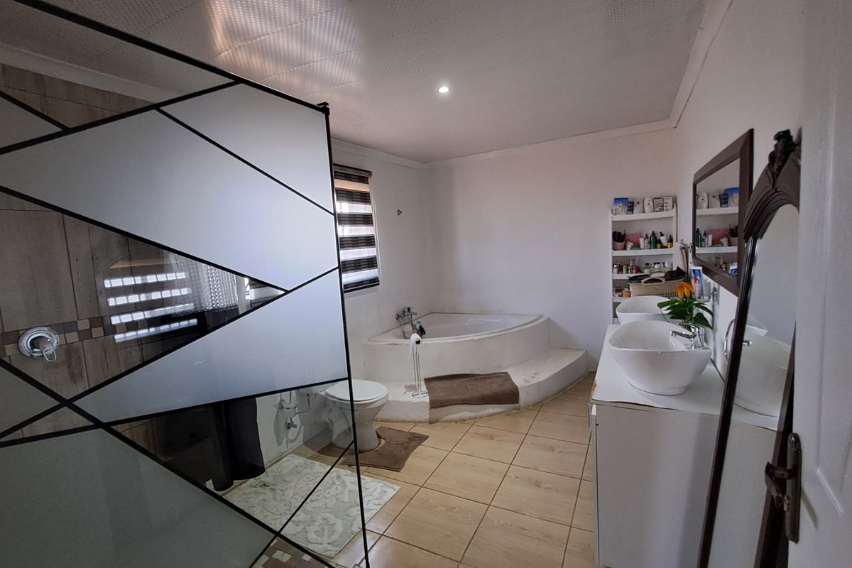 A spacious bathroom featuring a corner bathtub, dual vessel sinks on a vanity cabinet, and a modern geometric shower screen.