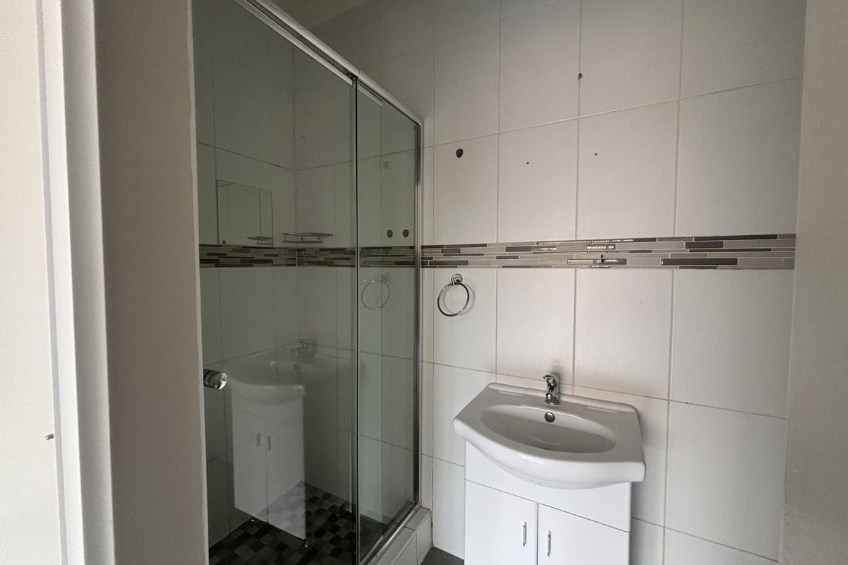 A compact bathroom featuring a glass shower enclosure and a vanity basin, currently requiring minor repairs to wall tiles and fixtures.