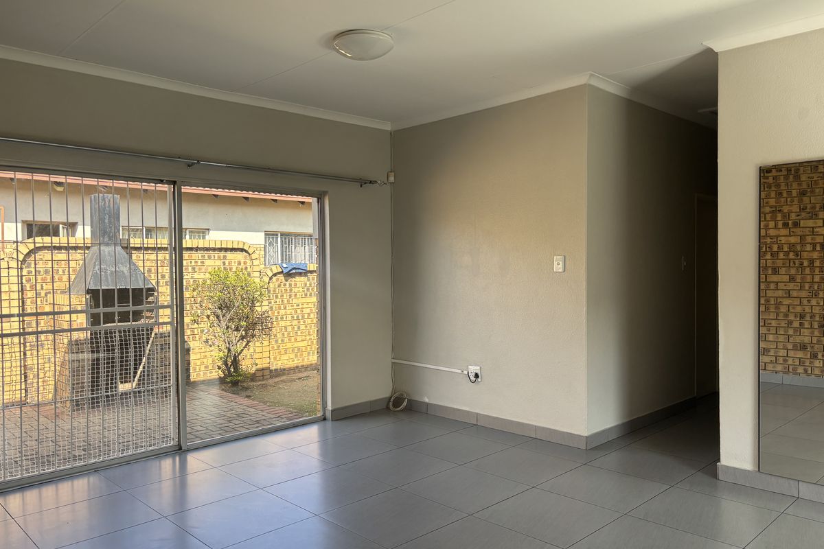 An empty living room featuring tiled floors, a neutral color palette, and a large sliding glass door providing access to the rear patio area.