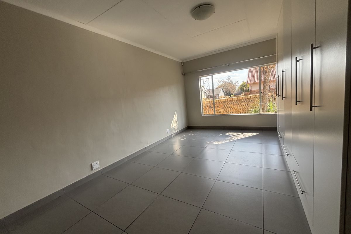 A bright, empty bedroom featuring neutral tiled flooring and extensive built-in cupboard storage, offering a clean and versatile space.