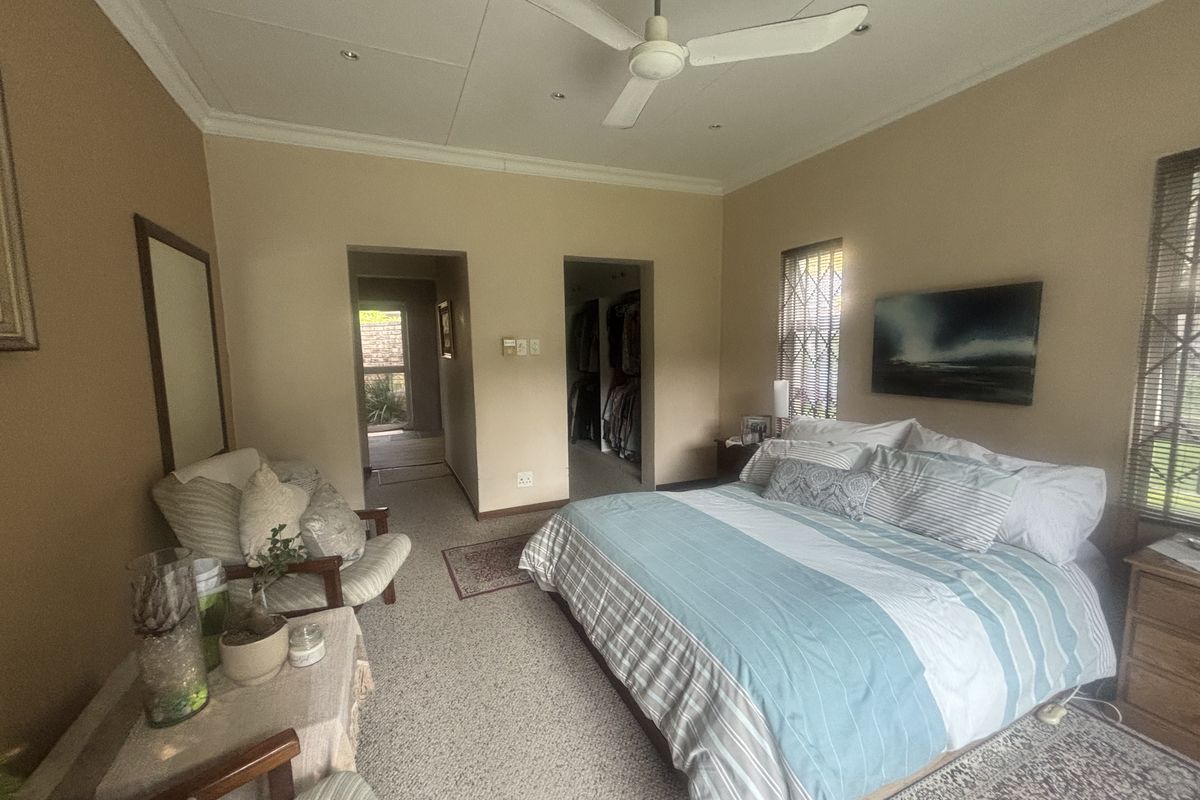 Spacious bedroom featuring neutral walls, carpeted flooring, a ceiling fan, and an adjoining walk-in closet area.