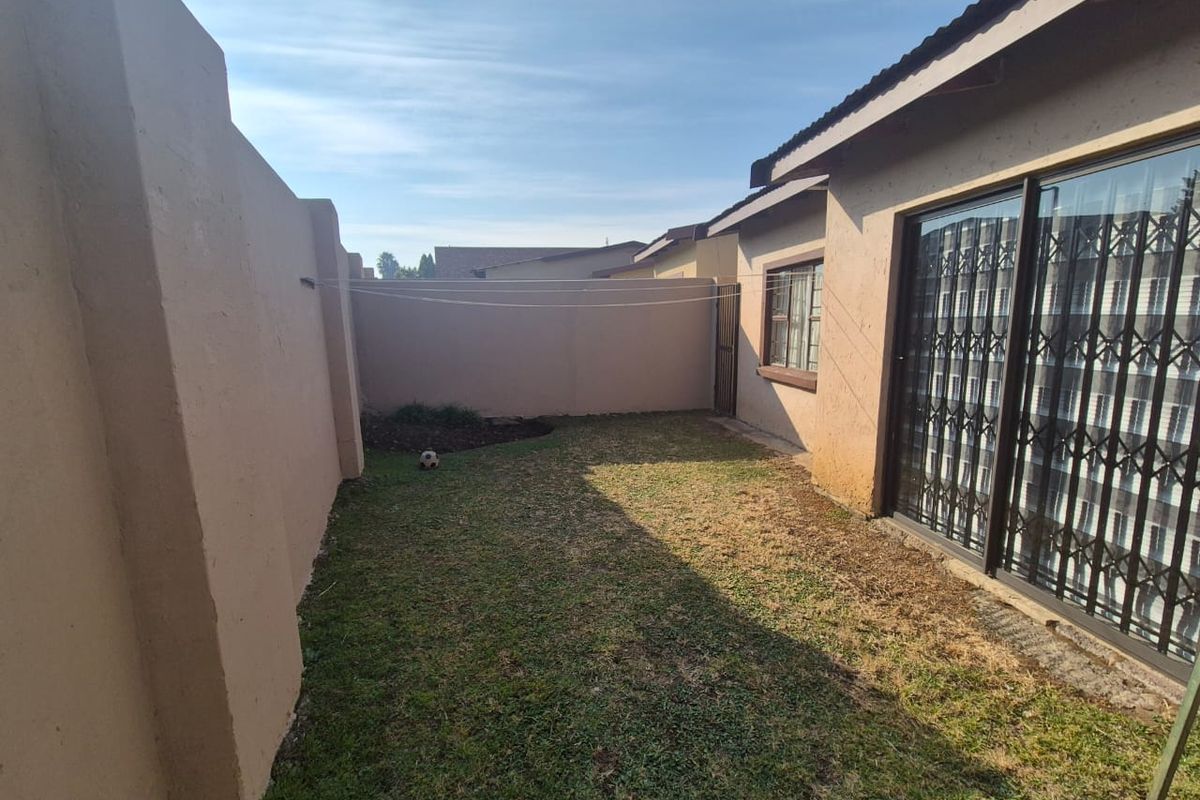 A private rear garden area featuring a lawn, perimeter boundary walls, and a sliding glass door with security gate access to the main dwelling.