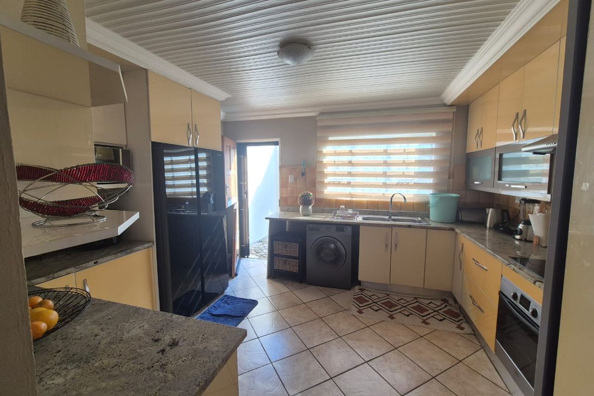 A functional kitchen featuring high-gloss cabinetry, granite countertops, integrated oven, and a dedicated space for laundry appliances with direct access to the exterior.