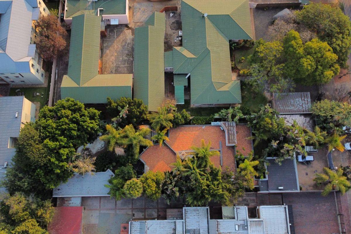 An aerial view of the property showing the roof structure, surrounding garden, paved driveway, and neighboring residential buildings.