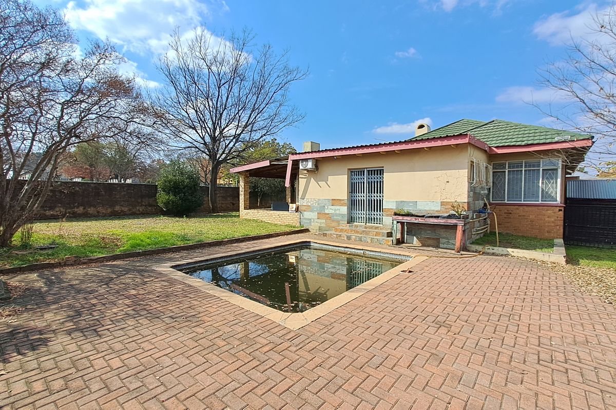 Rear exterior view featuring a paved patio area, a swimming pool, and a single-story house with tiled roofing and security features.