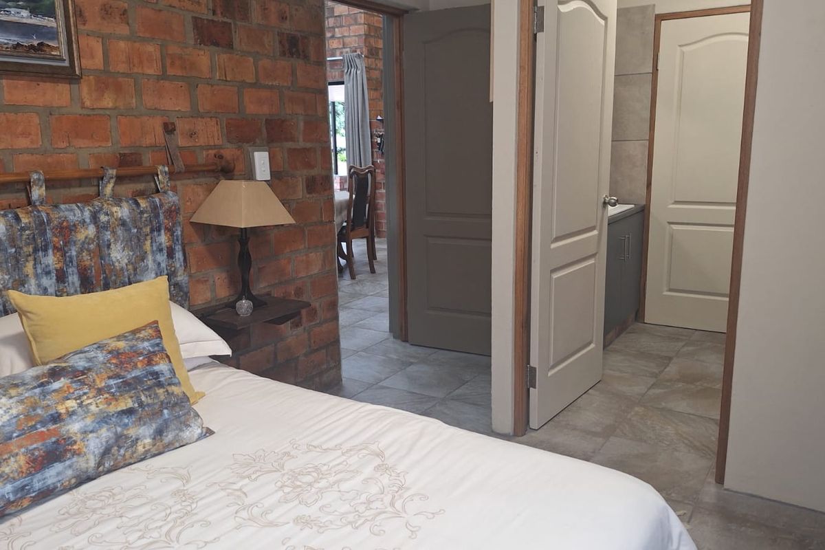 A bedroom featuring an exposed brick wall, tiled flooring, and direct access to an adjoining bathroom through panel doors.