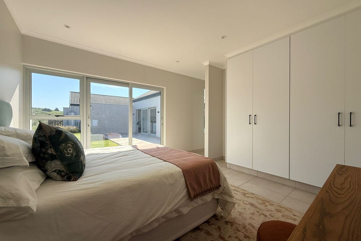 A bright bedroom featuring built-in cupboards, tiled flooring, and a large sliding glass door providing direct access to the outdoor area.