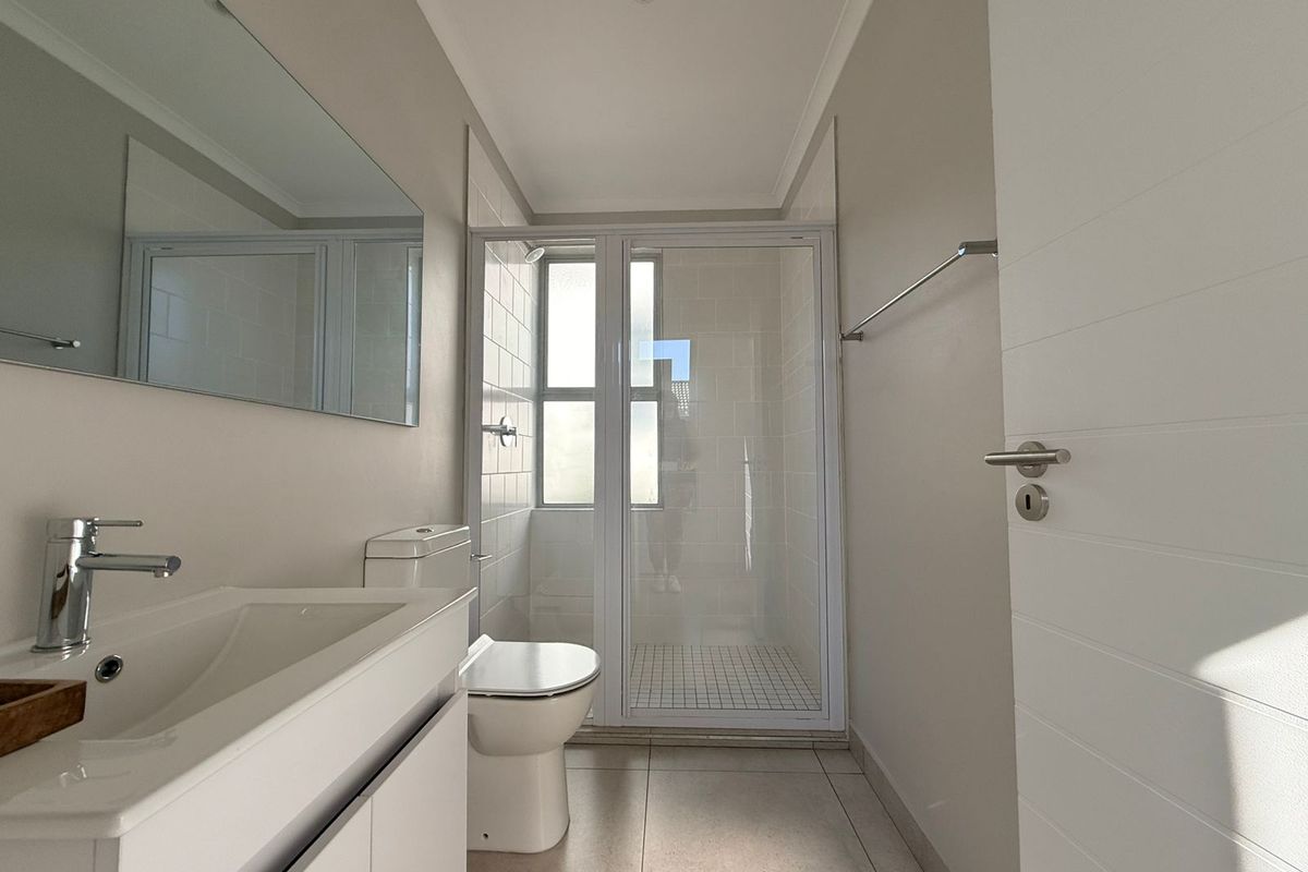 A clean, modern bathroom featuring a vanity with basin, toilet, and a glass-enclosed shower with tiled finishes.