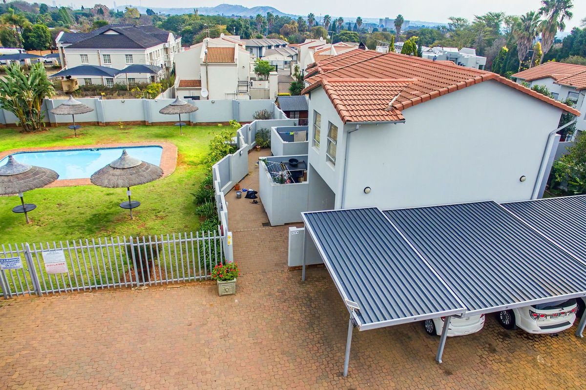 Aerial view of a townhouse complex featuring a communal swimming pool, landscaped garden areas, and covered carport parking bays.