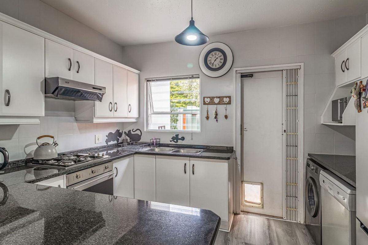 Functional kitchen featuring granite countertops, built-in oven, gas hob, extractor fan, and ample cabinetry with integrated laundry appliance space.