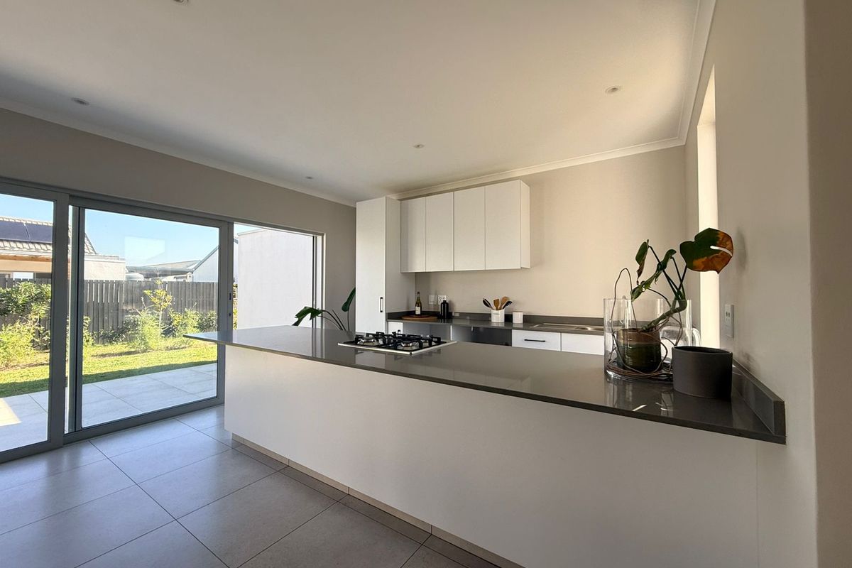 Modern kitchen featuring stone countertops, a gas hob, and sleek built-in cabinetry, with large sliding doors providing seamless access to the outdoor patio area.