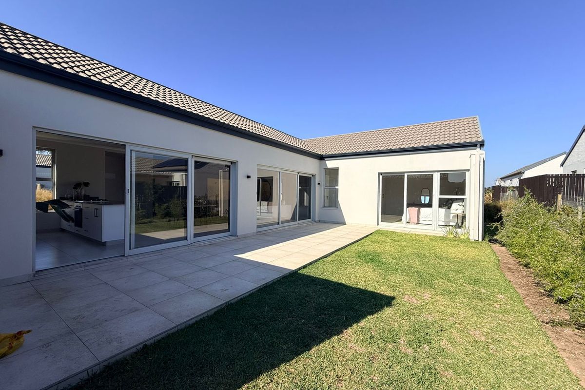 Rear view of the property featuring a paved patio area, large sliding glass doors providing indoor-outdoor flow, and a well-maintained lawn.