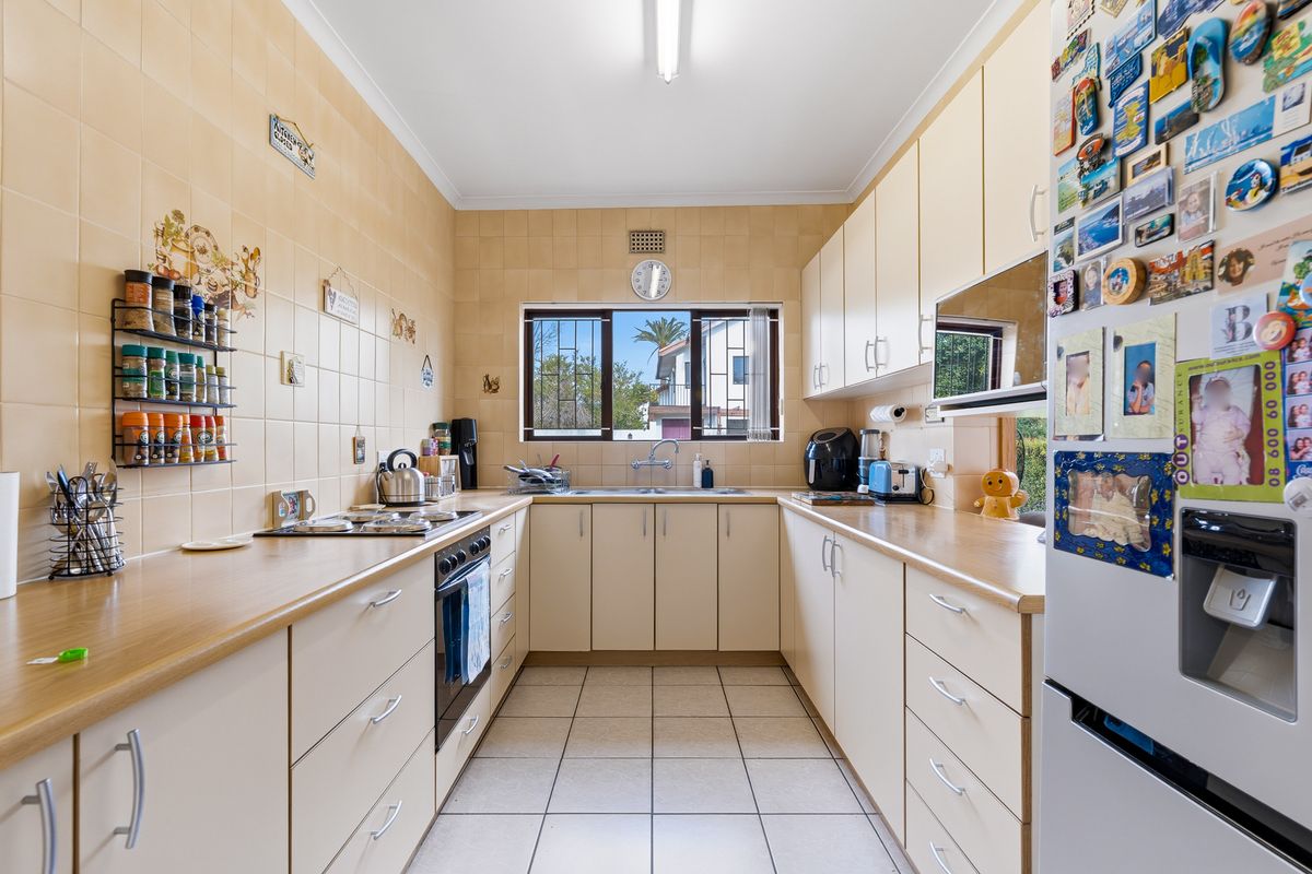 A functional U-shaped kitchen featuring laminate countertops, tiled backsplash, built-in cabinetry, and a stainless steel sink with a window view.