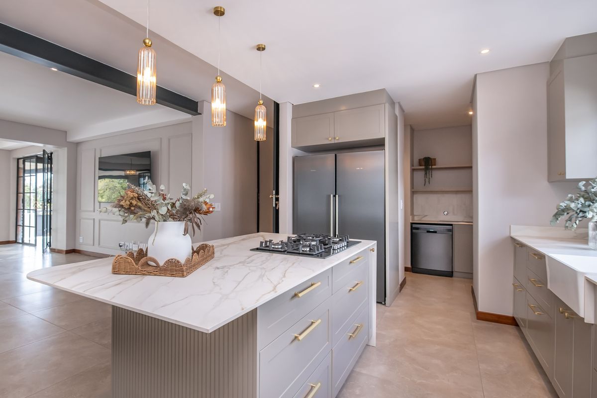 Modern kitchen featuring a marble-topped island with gas hob, farmhouse sink, custom cabinetry, and integrated appliances, flowing into an open-plan living area.