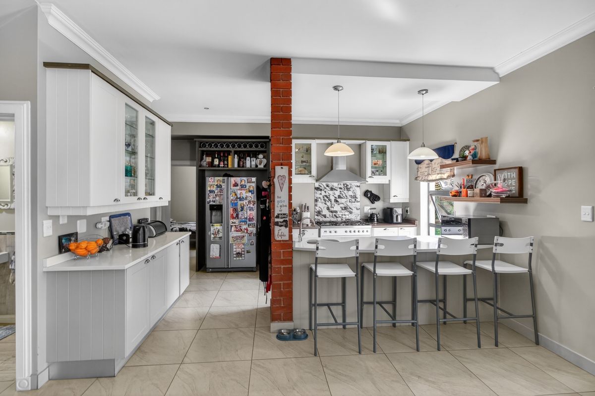 A well-lit kitchen featuring white cabinetry, stone countertops, a gas hob with extractor, and a central exposed brick pillar with a breakfast bar.