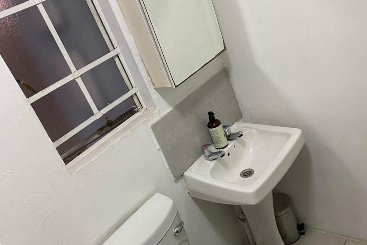 A compact bathroom featuring a pedestal basin, toilet, and mirrored medicine cabinet, with visible wall surface wear requiring maintenance.