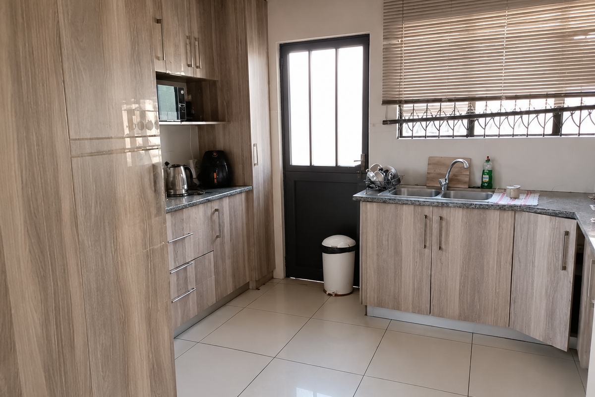 A functional kitchen featuring wood-look laminate cabinetry, granite countertops, a double sink, and tiled flooring with direct access to the exterior.