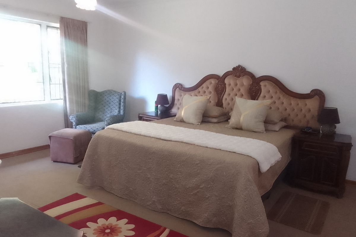 A spacious bedroom featuring carpeted flooring and a window with security bars, providing a functional and comfortable sleeping area.