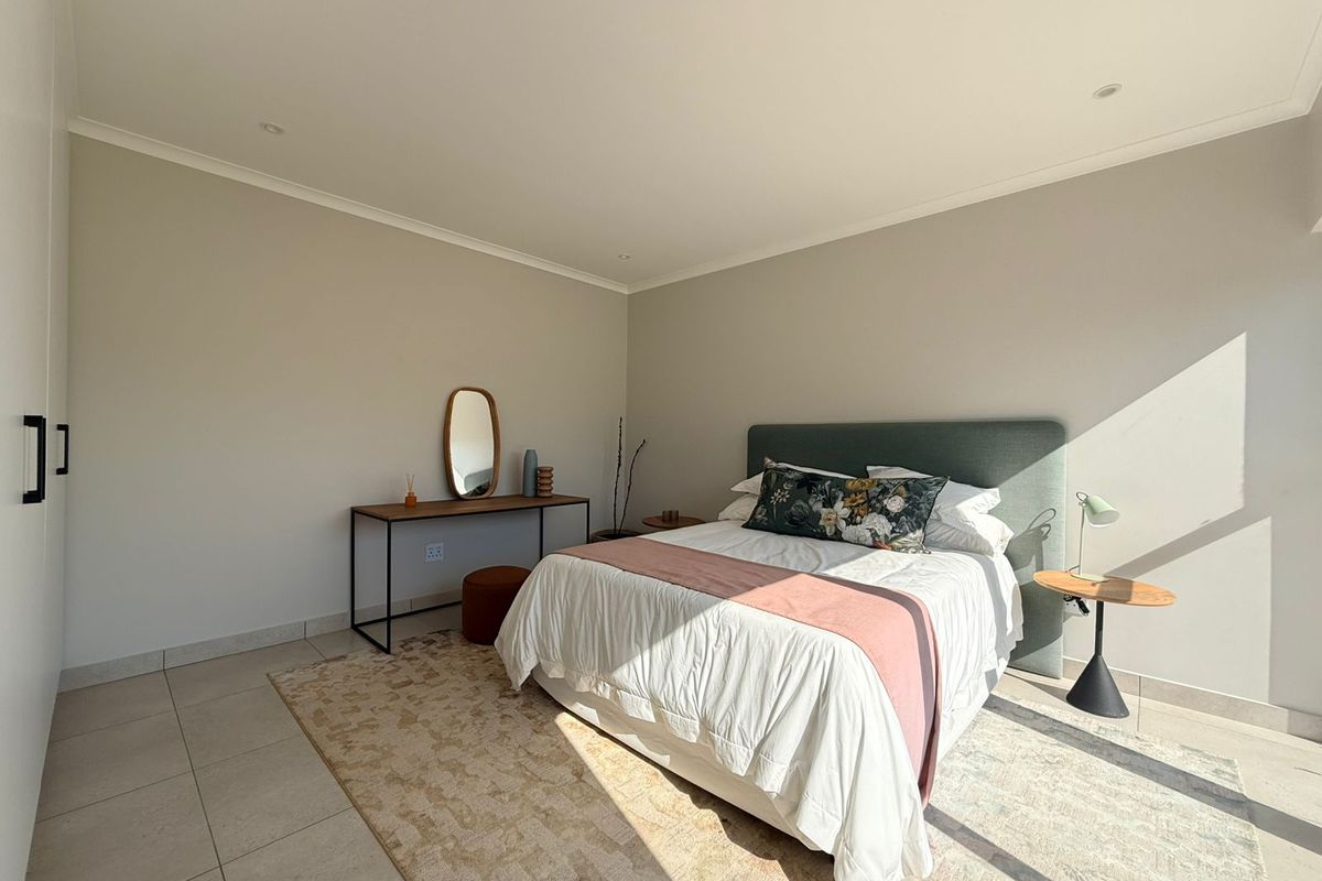 A bright and well-maintained bedroom featuring neutral walls, tiled flooring, recessed downlights, and ample built-in cupboard storage.